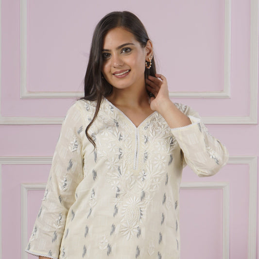 Woman wearing a white cable knit sweater in a room with a pink wall and wooden furniture.